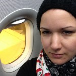 Eine junge Frau mit Beanie Mütze und Aspen Vista Halskrause sitzt in einem Flugzeug