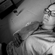 Eine Frau mit großer, schwarzer Brille liegt auf dem Boden mit einem Laptop auf ihren Beinen