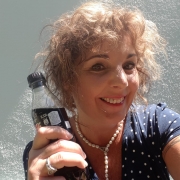 Eine Frau mit lockigen, hellbraunen Haaren trägt ein blaues Shirt mit weißen Polka-Dots und hält eine Cola Flasche in der Hand