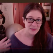 Ein Screenshot vom Interview mit Monica. Monica trägt eine schwarze Brille, hat langes, braunes Haar und sitzt in ihrem Arbeitszimmer
