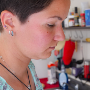 Nahaufnahme einer Frau mit kurzen, braunen Haare und vier Ohrringen beim Kochen in der Küche. Die Frau sieht unglücklich aus.