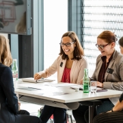 Vier junge Frauen sitzen um einen Tisch und führen ein Gespräch. Die Frauen lachen.