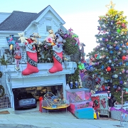 Tom & Jerry Weihnachtshaus in San Francisco: ein weißes viktorianisches Haus das bunt behängt mit Stofftieren ist. An der Terressa hängen zwei große rote Weihachtssocken mit den Worten Tom und Jerry. Rechts neben dem Haus steht ein riesiger Weihnachtsbaum mit bunten Kugeln und vor em Haus stehen verschiedene Miniaturspielzeuge, die sich bewegen, wie z. B. ein Miniaturvergnügungspark mit Achterbahn und eine Miniaturlokomotive die im Kreis fährt.