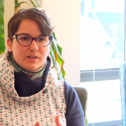 Karina, eine Frau mit kurzen, braunen Haaren und einer Blume im Haar gestikuliert und spricht in einem Interview.