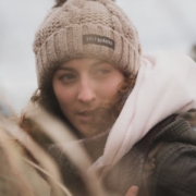 Lisa, eine Frau mit lockigen Haaren ist einem Feld. Sie trägt eine Wintermütze.