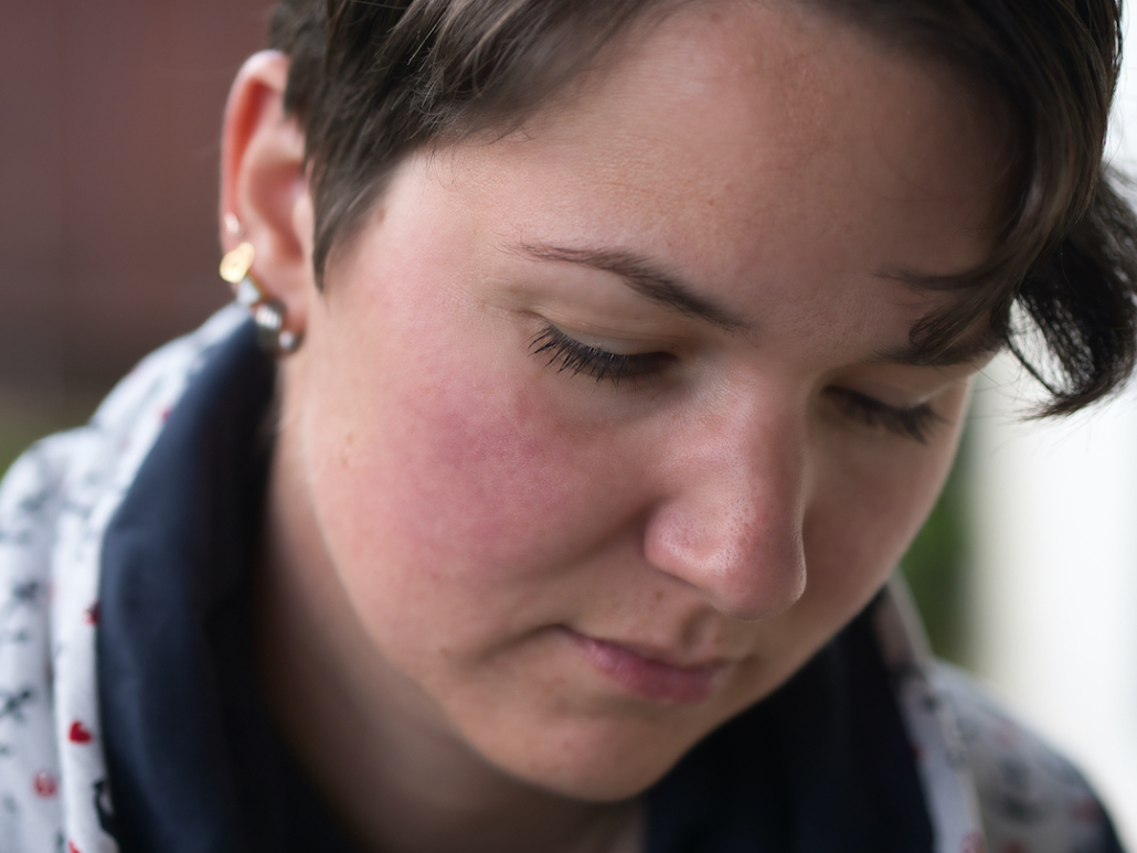Nahaufnahme von Karina's Gesicht. Karina hat kurze, brauen Haare und vier Ohrringe im rechten Ohr. Ihr Blick ist nach unten auf ein Buch hin gerichtet.