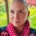 Karina, a woman with an almost shaved head stands in her garden. She wears a shirt with polka dots and a sweater with skulls.