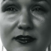 Schwarz-weiß Foto von Karina, einer Frau mit rasierten Haaren. Sie trägt Glitzerlidschaften und roten Lippenstift.
